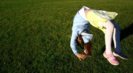 Girl in mid-air doing somersault on green grassの写真素材