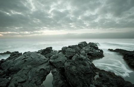 Tide coming in as blurred motion on a rocky beach during twilightの写真素材