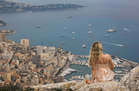 Young Blond Woman In Pink Dress Sits on Break. Aerial View of Monaco in The Background.の写真素材