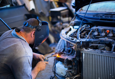 Welding industrial: worker in helmet repair detail in car auto service