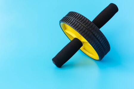 Yellow and Black Abs Roller Wheel on a Blue Background. Fitness Wheel isolated on a Blue Background. Copy Space for Textの写真素材
