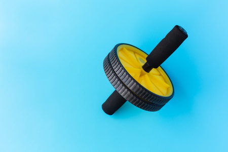 Yellow and Black Abs Roller Wheel on a Blue Background. Fitness Wheel isolated on a Blue Background.