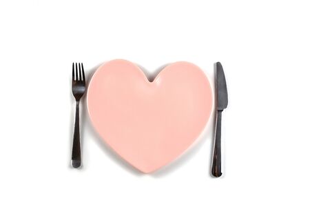 Plate in shape of heart, table knife and fork on white backgroundの写真素材