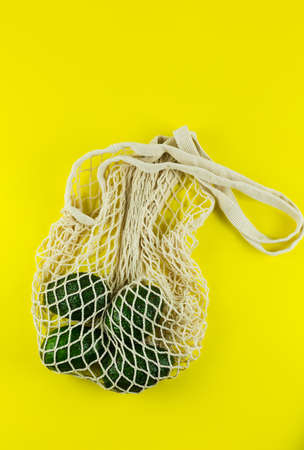 Avocado in a white eco net bag on a yellow background. Hass avocado in zero waste net bag. Plastic free concept. Copy Spaceの写真素材