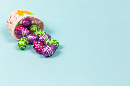 Colorful chocolate easter eggs in basket blue background. Small Chocolate eggs in a foil....