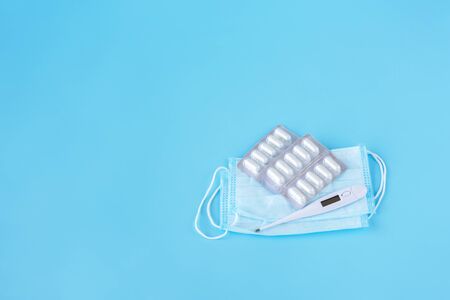 Face mask, thermometer, pills on a blue background. Medicine supplies for home coronavirus COVID-19 quarantine. Copy Spaceの写真素材