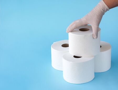 Female hand in medical gloves takes a roll of toilet paper from a folded tower of rolls on blueの写真素材