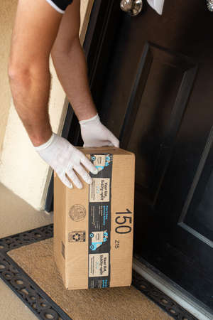 Miami, FL, USA - March 25, 2020: Amazon Prime package in a hands in at apartment door. Quarantine due Coronavirus. Amazon is an online company and is the largest retailer in the world.のeditorial素材