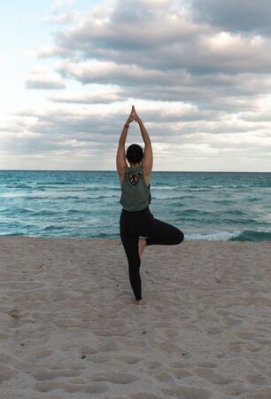 Attractive Woman doing yoga exercise at sandy beach, standing in Vrksasana Posture, Tree Pose. Woman standing on one leg in yoga pose. Copy Spaceの写真素材