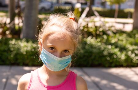 A little girl walks in the park in a medical face mask. A little girl walks through an empty city and covers her face with a mask from a coronavirus. Quarantine due Coronavirus time. Copy Space.の写真素材