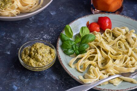 Tagliatelle cooked aldente with pasta pesto. Next to the bowl with sauces, a glass of fresh carrot. The noodles are decorated with green sprigs of basil. Healthy life experience. Proper nutrition.の写真素材