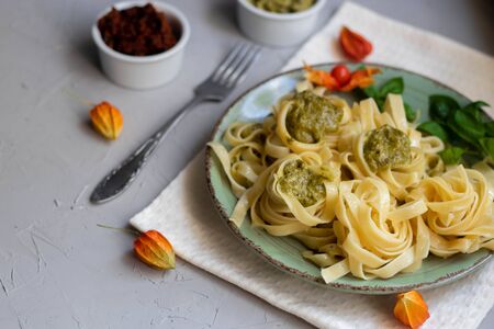 Tagliatelle cooked aldente with pasta pesto. Next to the bowl with sauces, a glass of fresh carrot. The noodles are decorated with green sprigs of basil. Healthy life experience. Proper nutrition.の写真素材