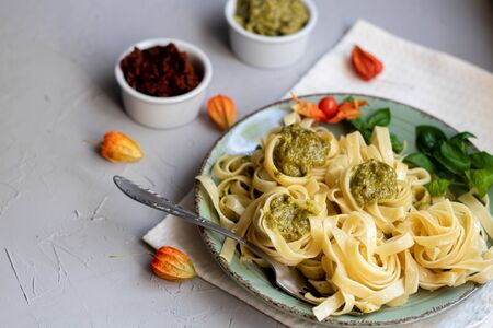 Tagliatelle cooked aldente with pasta pesto. Next to the bowl with sauces, a glass of fresh carrot. The noodles are decorated with green sprigs of basil. Healthy life experience. Proper nutrition.の写真素材