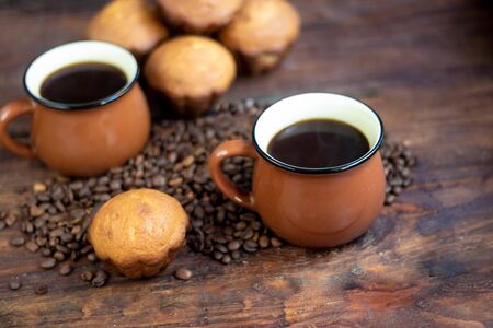 Coffee in brown cups. Hot, invigorating drink. Coffee beans are scattered nearby. In the background homemade cupcakes.の写真素材