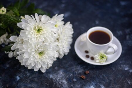 Bouquet of yellow chrysanthemums. Nearby is a cup of coffee, grains and a flower on a saucer, all on a dark background. Can be used for postcards.の写真素材