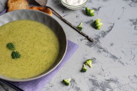 Detox green broccoli cream soup with chia seeds, red onions, green peppers, cherry tomatoes and croutons on a gray background. Healthy eating concept. Copy space.の写真素材