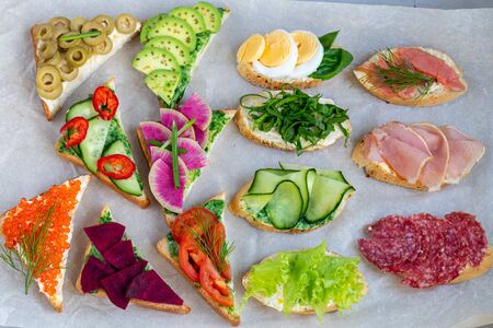Holiday sandwiches of various shapes. Vegetarian and more. Dressing with avocado and spinach and creamy yogurt. Top cucumber, turnips, tomatoes, salami, balyk, red caviar, spinach, eggs and olives.の写真素材