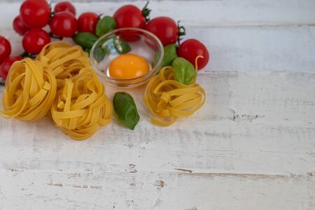 Ingredients for cooking Italian pasta. Pasta, basil, cheese, cherry tomatoes, olive oil, egg, yolk. On a light background. Copy space.の写真素材