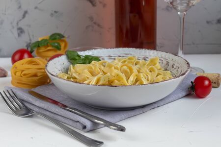 Italian pasta, spaghetti with avocado, basil, cream, cheese. Cherry tomatoes, olive oil. Meat with noodles. On a gray background. In the background is a glass of orange wine. Copy space.の写真素材