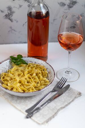 Italian pasta, spaghetti with avocado, basil, cream, cheese. Cherry tomatoes, olive oil. Meat with noodles. On a gray background. In the background is a glass of orange wine. Copy space.の写真素材