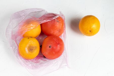 Environmentally harmful packages, spoiled fruits that lie in them. Ugly food. Copy space. Light background.の写真素材