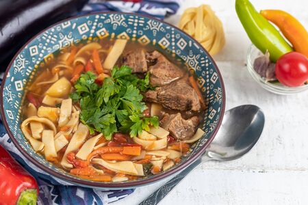 Eastern dish Lagman. Noodles, beef, blue, pepper, tomatoes. Hearty dish. Top decorated with parsley and cilantro. On a light background. Copy space.の写真素材