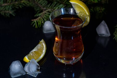 Turkish tea in a transparent glass with lemon slices. In the background is a Christmas tree branch. New Year. Black background. Copy space.の写真素材