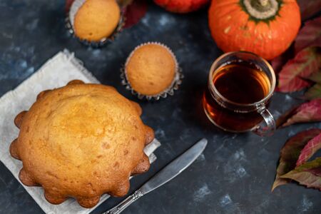 Big tasty cupcake for the holiday. Nelouin with pumpkin. Nearby is a transparent cup of hot, black tea. On a dark background.の写真素材