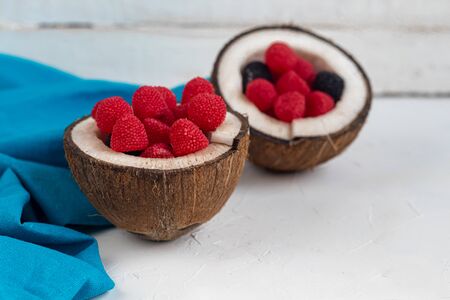 Red raspberries and blackberries in halves of a coconut. On white background. Copy space.の写真素材