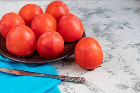 Large, orange persimmon fruits on a brown plate. On a gray, stone background. Copy space.の写真素材