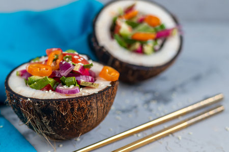 Fresh vegetables salad in coconut peel. Tomatoes, spinach, peppers, chili, radishes. On a gray,...