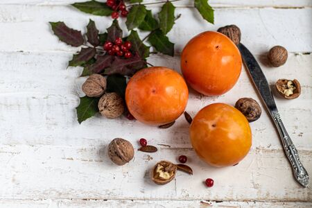 Persimmon on a light, wooden background. Near walnuts, viburnum berries. Winter fruit. Healthy eating Orange color. Copy space.の写真素材