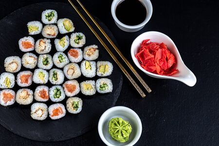 Sushi with fish, with cucumber, with eel, with avocado. Wrapped in Nori Seaweed. Food for vegetarians. Soy sauce, ginger, wasabi in white bowls. Copy space.の写真素材