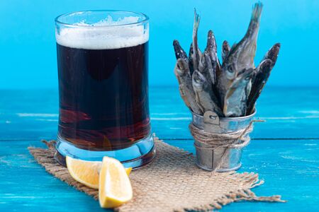 Small, salted fish with a glass of dark beer. Near the slices of lemon. Good snack for beer. Sea fish. Copy space. Background tinted in classic modern blue 2020.の写真素材
