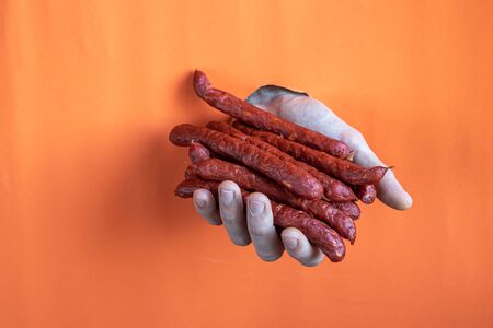 Male hand holds smoked sausages. Inserted into a hole in a piece of paper. Copy space.の写真素材