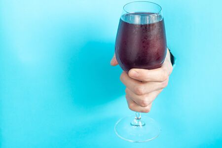 Male hand holds a glass with red wine. Inserted into a hole in a piece of paper. Copy space.の写真素材