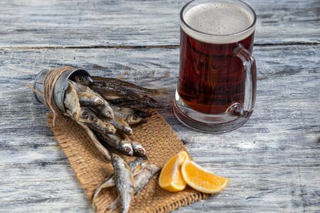 Small, salted fish with a glass of dark beer. Near the slices of lemon. Good snack for beer. Sea fish. Copy space. On a light, wooden background.の写真素材