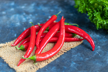 Hot red chili peppers on a dark background under concrete. Spicy food supplement. Parsley and...
