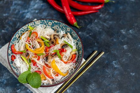 Oriental rice noodles Udon with sweet pepper, mushrooms. On a dark background. Near chopsticks. A dish sprinkled with sesame seeds. Copy space.の写真素材