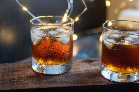 Whiskey in glasses with ice and perspiration on a dark background. A row of tangerines. Festive...