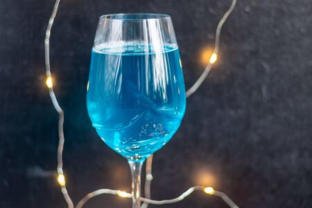 Blue wine in a glass on a dark background. In the background bokeh of lights. Festive mood. New Year. Copy space.の写真素材