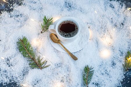 White cup with hot coffee. Stands in artificial snow. Near a branch of spruce. New Year's and Christmas. Copy space.の写真素材