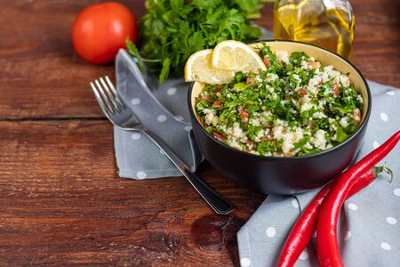 Tabule salad in a round plate on a wooden background. Couscous, parsley with green onions and tomatoes and mint. Dressed with olive oil and lemon juice. Copy space.の写真素材