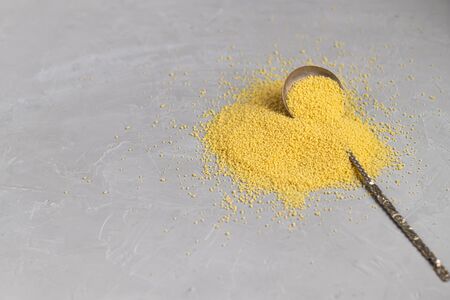 Cous Cous is scattered on a gray background under concrete. On it lies a spoon, which measures the number. Healthy food. Vegetarianism. Copy space.の写真素材