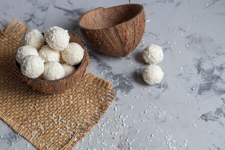 Candies in coconut flakes and fresh coconut with flax seeds on a gray stone background. Energy balls. Copy space.の写真素材