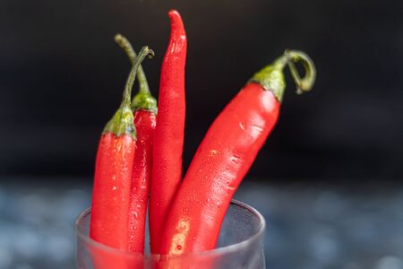 Bright red ripe chili peppers in a transparent glass on a dark blue surface under concrete. Trend of color 2020. Copy space.の写真素材