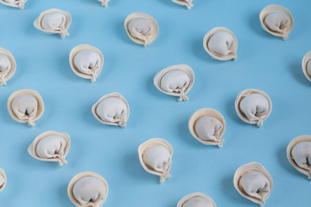 A pattern of raw, frozen dumplings on a light blue background. View from above.