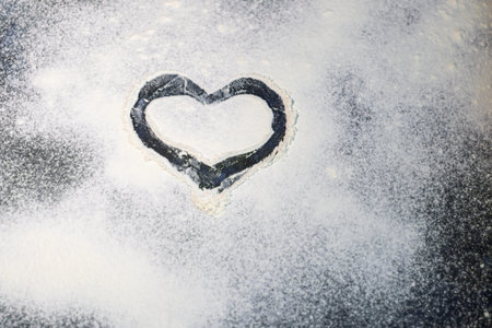 Flour is sprinkled on the table. They draw a heart on it with a finger. Valentine's Day. Dark...