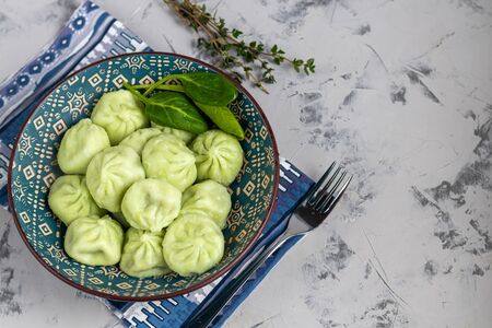 Boiled khinkali made of dough with spinach. Garnished with Red Chilli, Dill and Parsley. On a light gray background under. Raw khinkali frozen on a wooden board next to it. Copy space.の写真素材