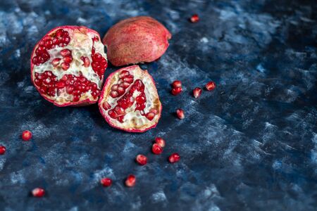 Large pomegranate broken into pieces. On a blue background under a stone. Trend 2020. Grains are scattered nearby. Copy space.の写真素材